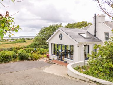 Exterior of a white house with large windows and a garden path at The Mermaid in Dungloe County Donegal
