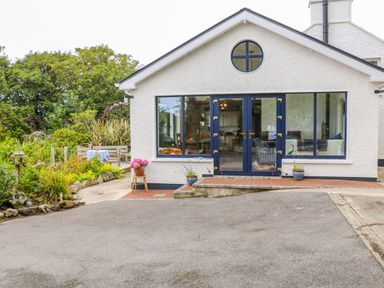 Exterior view of a white house with blue doors and windows surrounded by plants and a paved driveway at The Mermaid in Dungloe County Donegal