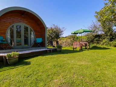 A garden with a wooden pod structure and outdoor seating under a green umbrella at The Lamb Shack in St Teath
