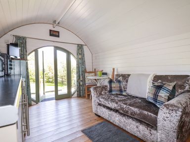 A small living space with a sofa, pillows, a small table with chairs, and a set of large double doors opening to the outside at The Lamb Shack in St Teath