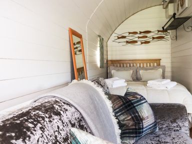 A small bedroom with a bed pillows blankets a mirror on the wall and a sofa with cushions at The Lamb Shack in St Teath