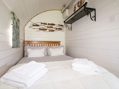 A bedroom with a wooden bed frame and bed with pillows and folded towels on top at The Lamb Shack in St Teath