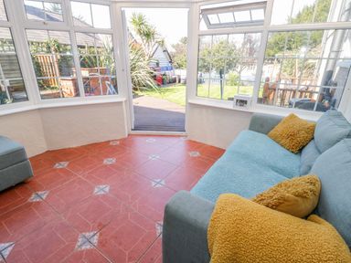 A sunroom with a blue sofa and yellow pillows overlooking a garden at Penholm in Penmaenmawr