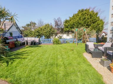A garden with lawn furniture a swing set a barbecue and green bushes at Penholm in Penmaenmawr