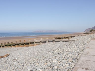 A pebble beach with wooden groynes along the shoreline and a paved walkway at Penholm in Penmaenmawr