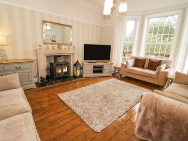 A living room with beige sofas a television on a cabinet a fireplace and large windows at Penholm in Penmaenmawr