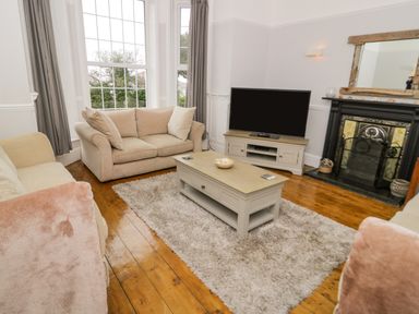 A living room with two beige sofas a wooden coffee table and a TV on a stand at Penholm in Penmaenmawr