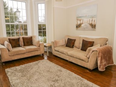 A living room with two beige sofas a wooden floor a beige rug and a painting on the wall at Penholm in Penmaenmawr