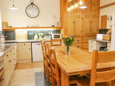 A kitchen with wooden dining table and chairs a large wall clock and wooden cupboards at Penholm in Penmaenmawr