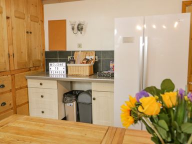 A kitchen with wooden cabinets a white refrigerator a countertop with a basket and a welcome sign and flowers in the foreground at Penholm in Penmaenmawr