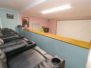 A home theater room with black leather recliners and a large projection screen at Penholm in Penmaenmawr