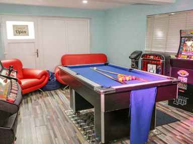 A game room with a pool table two red sofas arcade machines and a door with an open sign at Penholm in Penmaenmawr