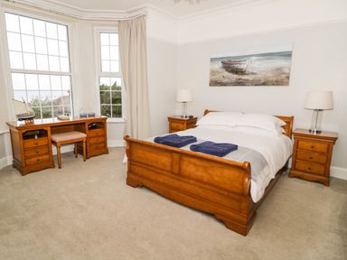 A bedroom with a wooden bed and two nightstands with lamps next to a window with a wooden desk and chair at Penholm in Penmaenmawr