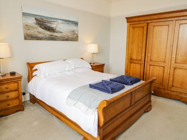 A bedroom with a wooden bed frame white bedding two bedside tables with lamps and a large wooden wardrobe at Penholm in Penmaenmawr