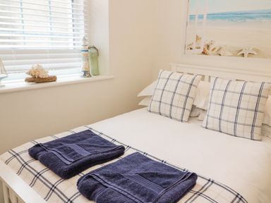 A bed with two folded dark towels on a checkered bed runner and checkered pillows with a window and a beach themed picture in a bedroom at Penholm in Penmaenmawr