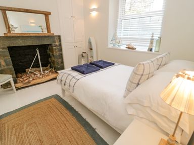 A bedroom with a bed with pillows and towels near a stone fireplace and window at Penholm in Penmaenmawr