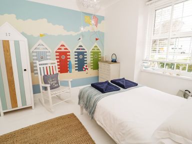 A bedroom with a bed white rocking chair wardrobe chest of drawers and a window with blinds at Penholm in Penmaenmawr