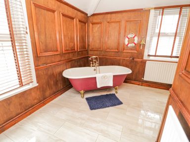 A bathroom with a freestanding bathtub a blue bath mat wooden panel walls and two windows with blinds at Penholm in Penmaenmawr