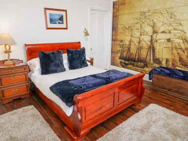A bedroom with a wooden bed frame two dark pillows folded towels bedside table with lamp and a large wall mural of a ship at Penholm in Penmaenmawr