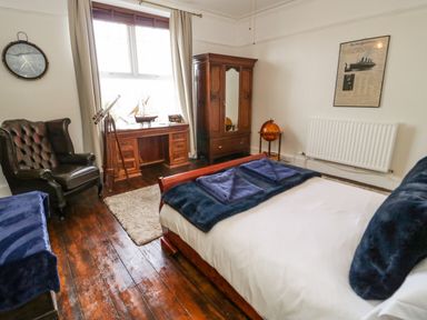 A bedroom with a bed a wooden desk a leather armchair and a wooden wardrobe at Penholm in Penmaenmawr