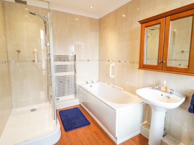 A bathroom with a shower enclosure a bathtub a pedestal sink a wall cabinet and a blue bath mat at Penholm in Penmaenmawr