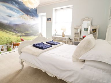 A bedroom with a white bed two folded towels a dresser a vanity mirror and a mural of a mountain landscape at Penholm in Penmaenmawr