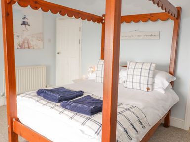 A bedroom with a wooden four-poster bed with checked cushions and folded towels on the bed at Penholm Penmaenmawr