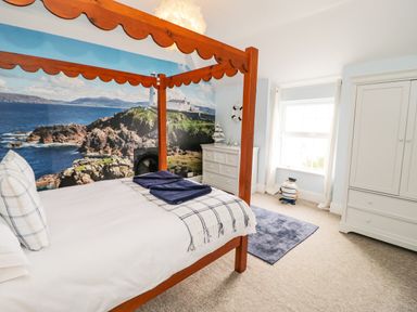 A bedroom with a wooden canopy bed and a lighthouse mural on the wall at Penholm in Penmaenmawr