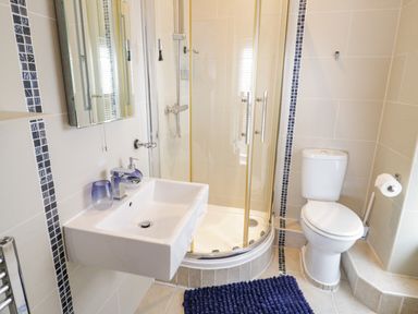 A bathroom with a wall-mounted sink a glass-enclosed shower a toilet and a dark blue bath mat at Penholm Penmaenmawr
