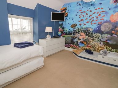 A bedroom with a single bed a small boat-shaped bed a white dresser a television and an underwater sea fish mural on the wall at Penholm in Penmaenmawr