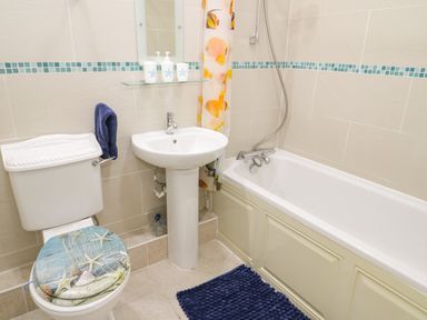 A bathroom with a toilet a pedestal sink a bathtub with a shower curtain and a blue bath mat at Penholm in Penmaenmawr