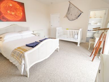 A bedroom with a double bed a baby crib a telescope and a door leading to a bathroom at Penholm Penmaenmawr
