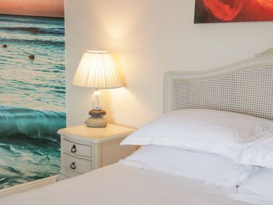 A bedroom with a bedside table lamp and a bed with white pillows and a wicker headboard at Penholm in Penmaenmawr