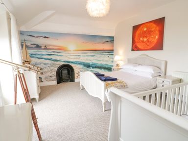A bedroom with a white bed a crib two nightstands a telescope a lamp and a large ocean sunset mural at Penholm in Penmaenmawr