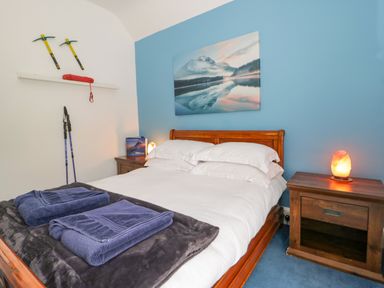 A bedroom with a wooden bed with white bedding blue walls and hiking equipment on the wall at Penholm in Penmaenmawr