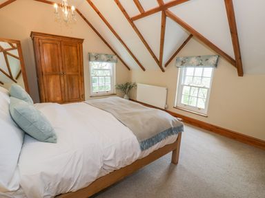 A bedroom with a wooden bed with pillows and blanket a wooden wardrobe two windows with floral blinds and exposed wooden ceiling beams at Llety Perygl in Harlech