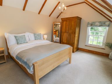 A bedroom with a wooden bed a wooden wardrobe a full length mirror a window with a floral blind and a chandelier at Llety Perygl in Harlech