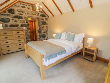 A bedroom with a wooden bed a wooden dresser and a wooden nightstand with a lamp at Llety Perygl in Harlech