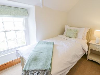A bedroom with a single bed next to a window and a nightstand with a lamp at Llety Perygl Harlech