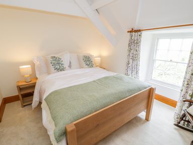A bedroom with a wooden bed frame green throw and floral curtains at Llety Perygl in Harlech