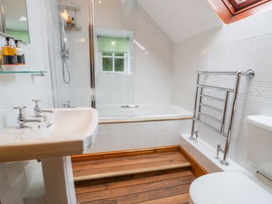 A bathroom with a bathtub shower sink toilet towel rail and wooden flooring at Llety Perygl in Harlech