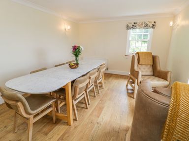 A dining room with a long marble table surrounded by wooden chairs and two armchairs with blankets at Llety Perygl in Harlech