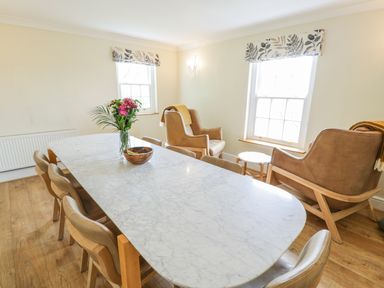 A dining room with a marble table a flower vase wooden chairs and two armchairs by windows at Llety Perygl in Harlech