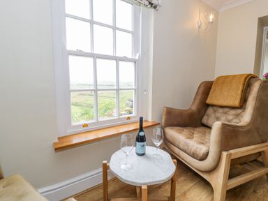 A seating area with a brown armchair a small round table with a bottle and two wine glasses next to a large window at Llety Perygl in Harlech