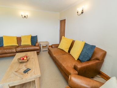 A living room with two brown leather sofas with yellow and blue cushions and a wooden coffee table with a fruit bowl at Llety Perygl in Harlech