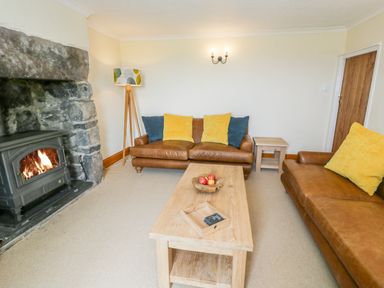 A living room with leather sofas yellow and blue cushions a wooden coffee table and a stone fireplace at Llety Perygl in Harlech