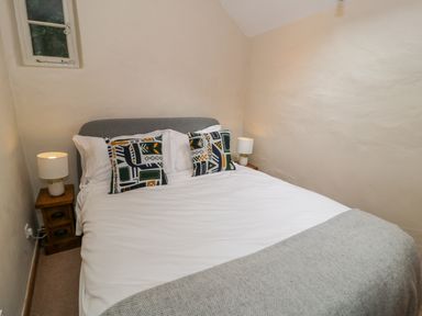 A bedroom with a double bed white sheets grey blanket patterned pillows wooden bedside tables and lamps at Llety Perygl in Harlech