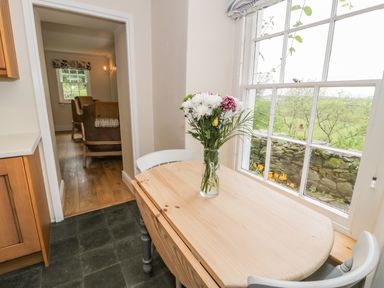 A kitchen with a wooden table and a vase of flowers by a window overlooking a garden at Llety Perygl in Harlech