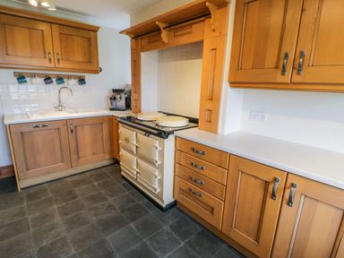 A kitchen with wooden cabinets a double sink a coffee machine and a cream oven at Llety Perygl in Harlech
