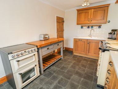 A kitchen with a stove toaster wooden cabinets and a sink at Llety Perygl in Harlech